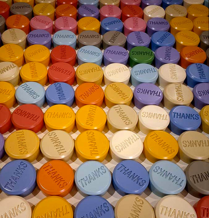 Colorful round tokens embossed with the word THANKS in various pastel and bright colors arranged in rows