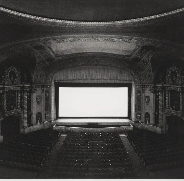 Vintage black and white photo of ornate classic movie theater interior with large blank screen and empty seats